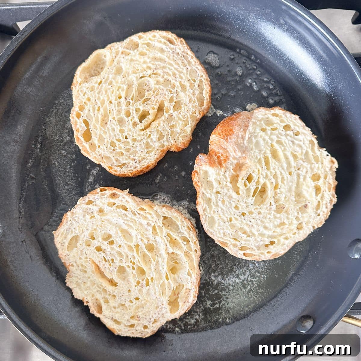 Pâtisserie French Toast 5 A skillet on medium heat with melted butter, and uncooked croissant halves being placed into it after dipping in egg mixture.