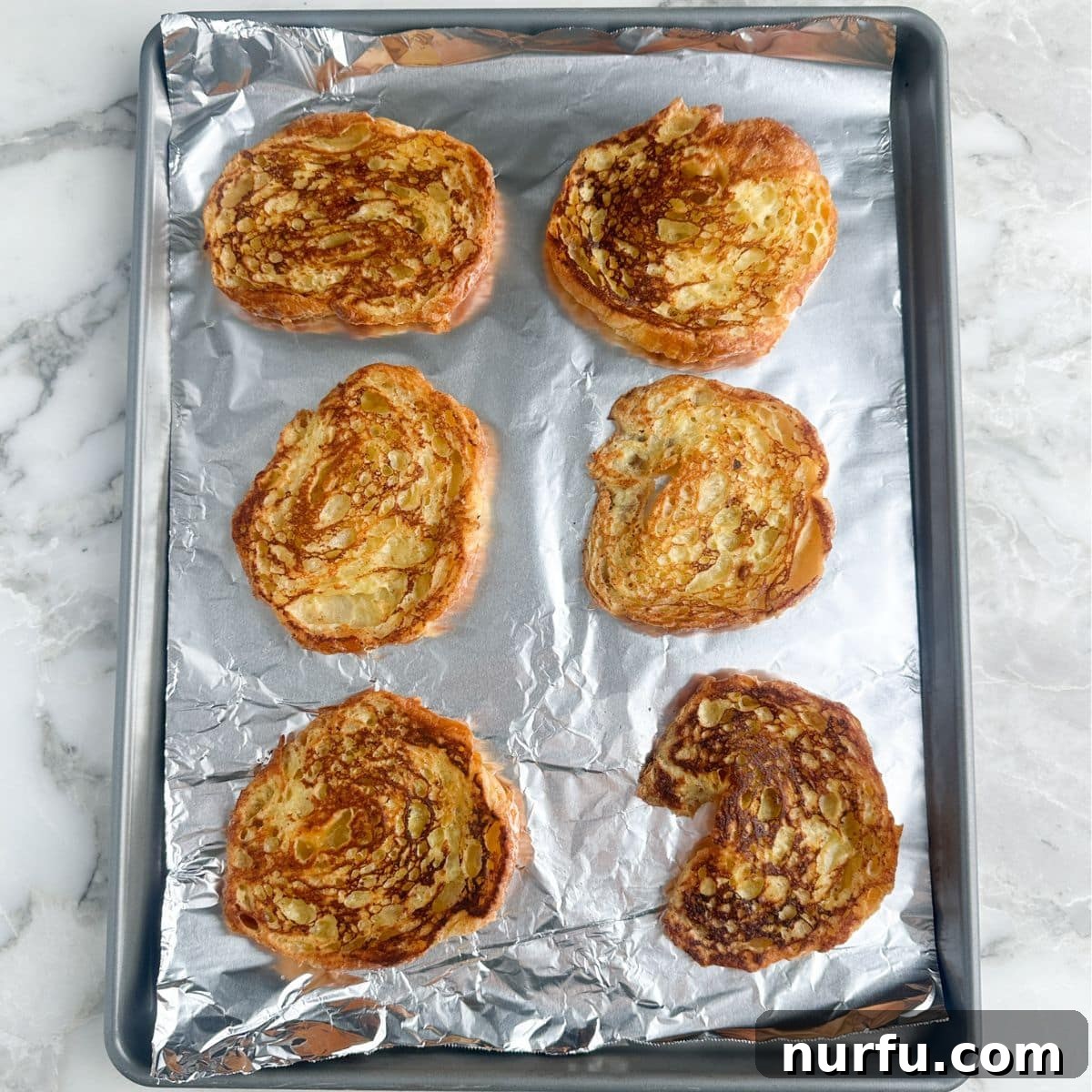 Pâtisserie French Toast 6 A pan filled with perfectly cooked, golden-brown croissant French toast halves.