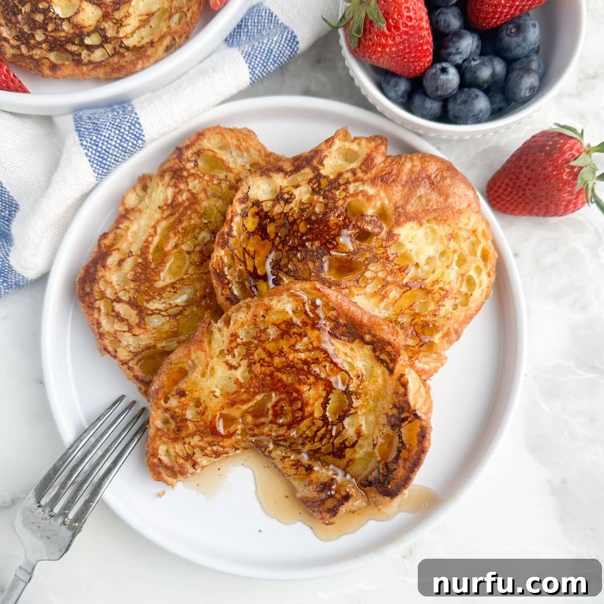 Pâtisserie French Toast 7 A plate of golden-brown croissant French toast, generously drizzled with maple syrup.