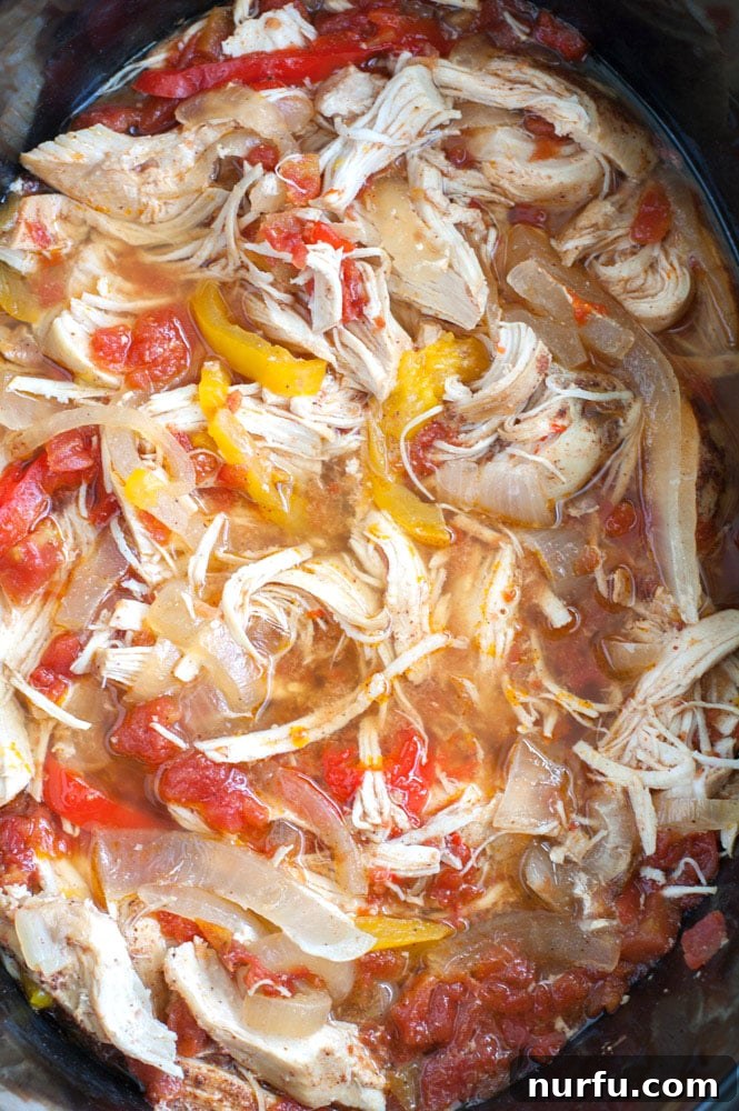 Cooked chicken strips with softened bell peppers and onions simmering in a slow cooker, ready to be served.