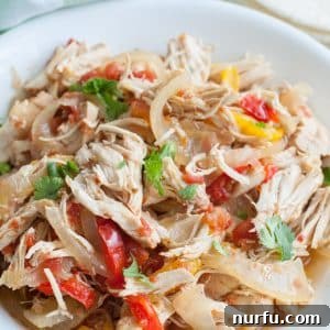A bowl with shredded chicken, colorful onions and bell peppers, a delicious Crockpot Chicken Fajitas serving.