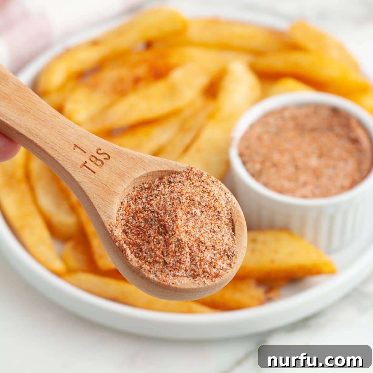 The Crimson Kitchen Blend 6 A tablespoon of Red Robin seasoning held over a plate of perfectly seasoned fries.