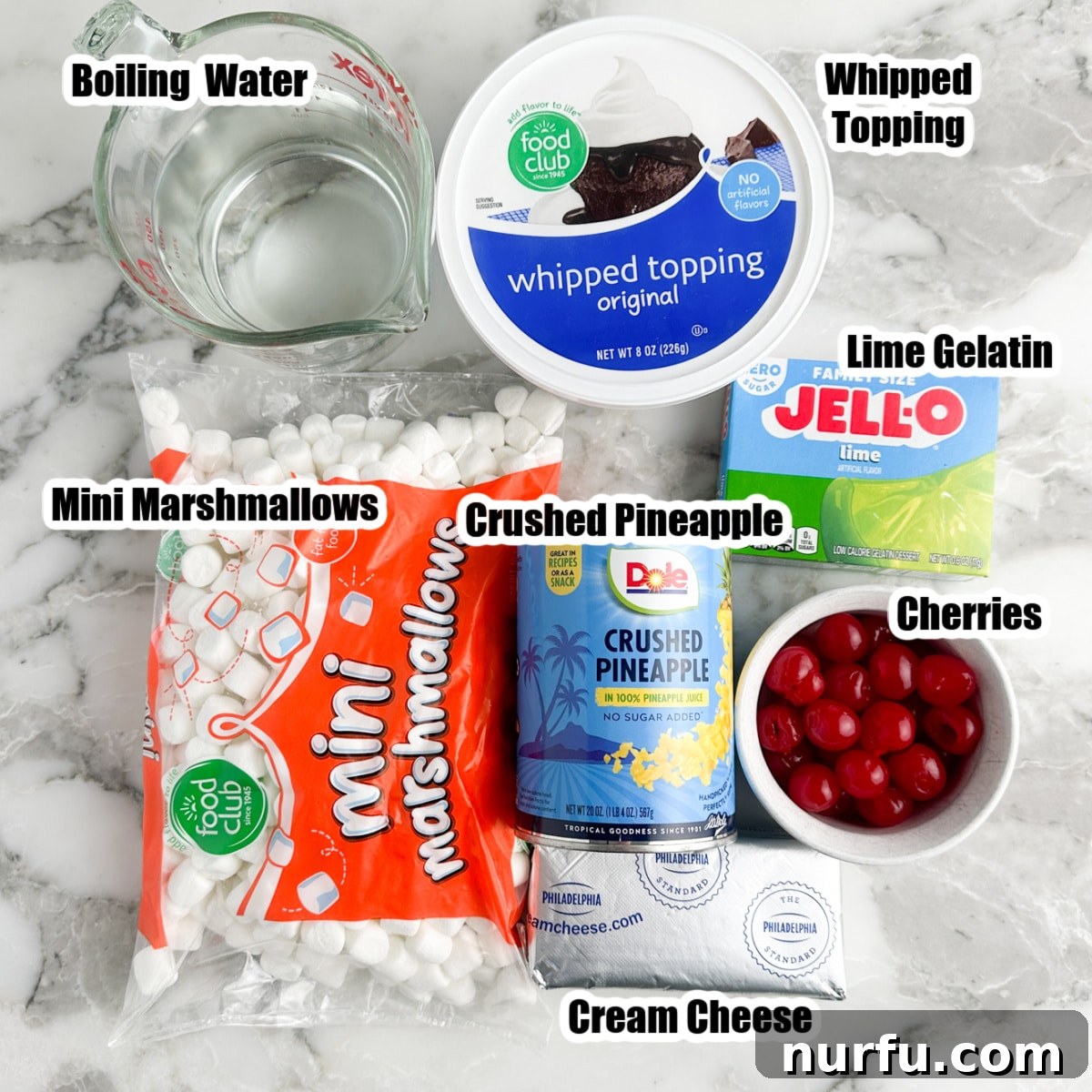 Sea Mist Salad 3 A selection of ingredients for sea foam salad: a bag of mini marshmallows, a can of crushed pineapple, a bowl of maraschino cherries, a block of cream cheese, and a tub of whipped topping, arranged on a rustic wooden surface.