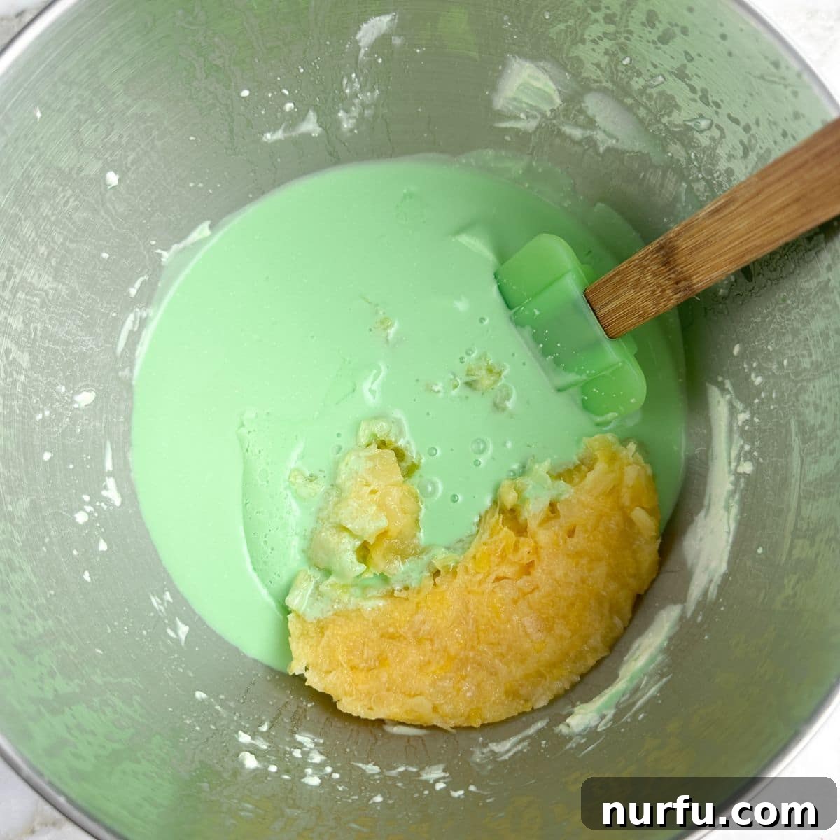 Sea Mist Salad 5 A mixer bowl with the green jello and cream cheese mixture, now with crushed pineapple stirred in, showing a slightly chunkier texture.