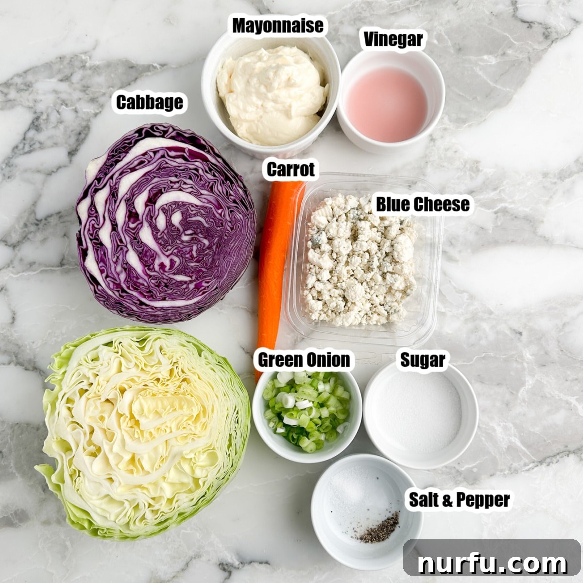 Bold Blue Coleslaw 3 A selection of fresh ingredients laid out for making blue cheese coleslaw, including vibrant red and green cabbage, a bowl of creamy mayonnaise, clear vinegar, shredded carrots, chopped green onions, a block of blue cheese, and a sprinkle of sugar.
