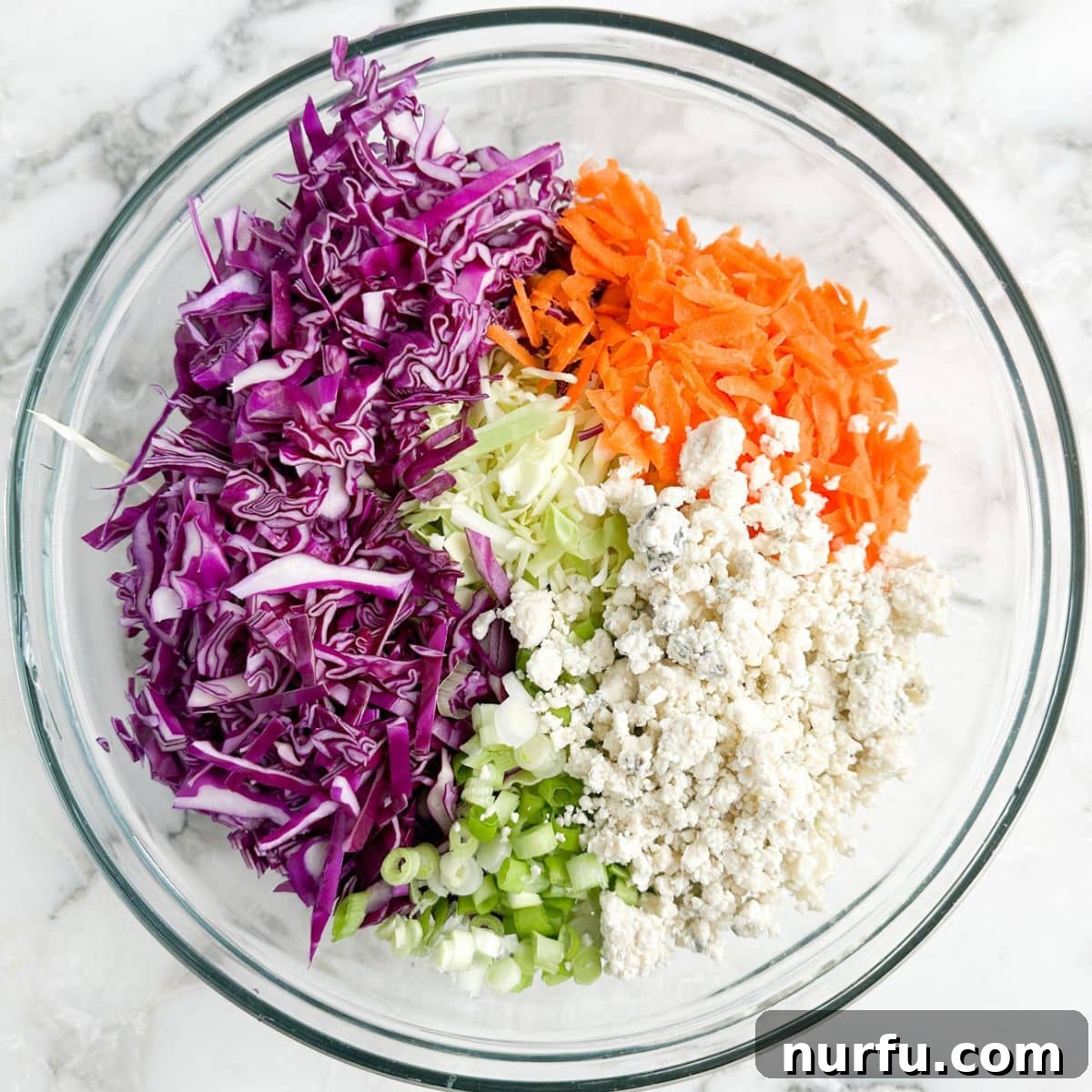 Bold Blue Coleslaw 5 A large mixing bowl filled with a colorful medley of shredded red and green cabbage, bright orange carrots, and generous crumbles of pungent blue cheese, ready for the dressing.