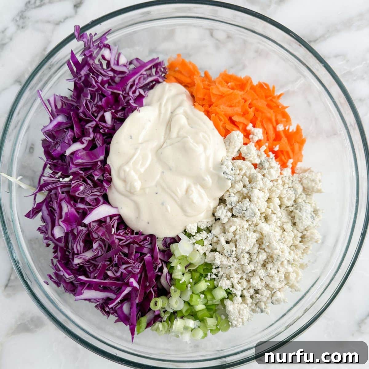 Bold Blue Coleslaw 7 The creamy blue cheese dressing being poured generously over the vibrant mixture of cabbage, carrots, and blue cheese crumbles in a large bowl, ready for tossing.
