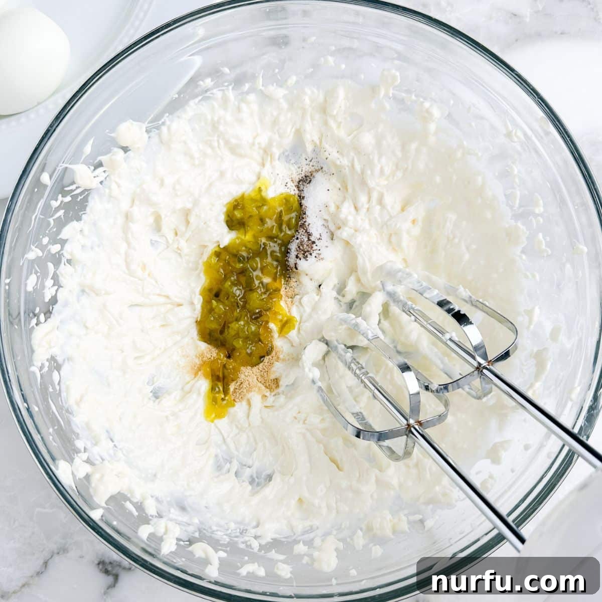 Savory Whipped Egg Dip 4 Close-up shot of mayonnaise and relish being mixed in a bowl with an electric mixer, creating the creamy base for the deviled egg dip, highlighting the smooth texture.
