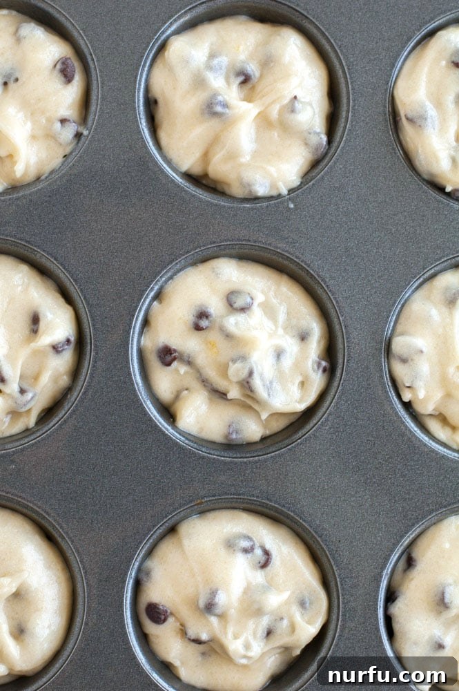 Prepping Mini Chocolate Chip Muffins Mini chocolate chip muffin batter being scooped into a mini muffin pan.