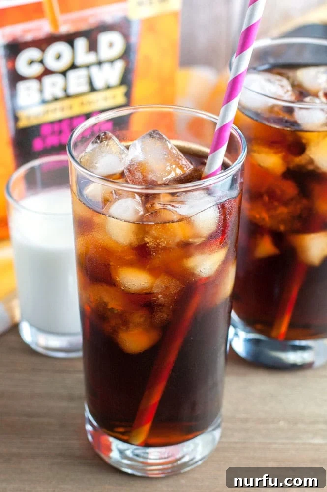 Tall glass of iced coffee with pink straw, garnished with mint, on a wooden surface.