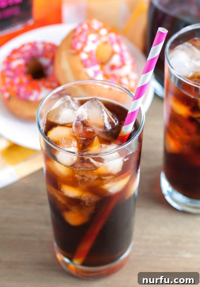 A glass of cold brew coffee served with two glazed donuts on a wooden tray.