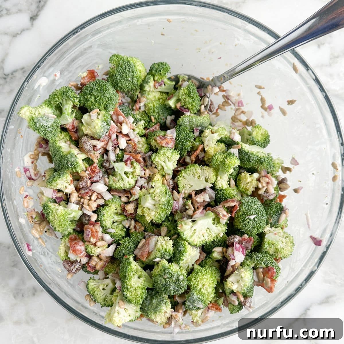 Vibrant Broccoli Raisin Bliss 5 A close-up of a large bowl filled with freshly prepared broccoli raisin salad, showing the creamy dressing coating all ingredients, including green broccoli, red onion, golden raisins, and brown bacon bits.