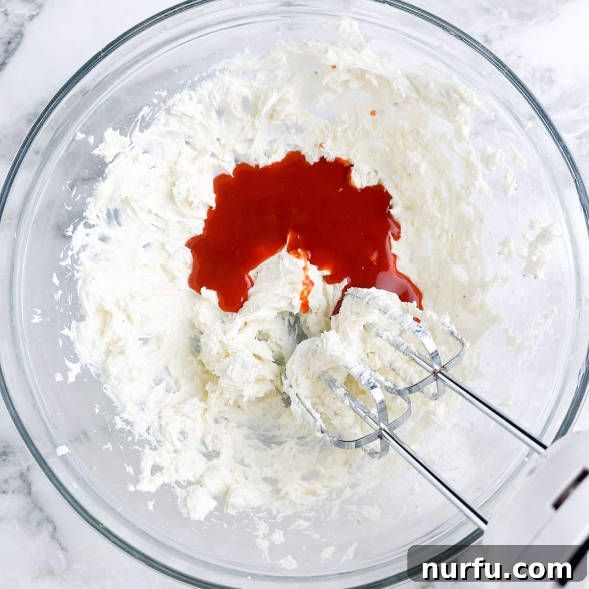 A bowl containing softened cream cheese, buffalo sauce, and ranch seasoning, ready to be mixed.