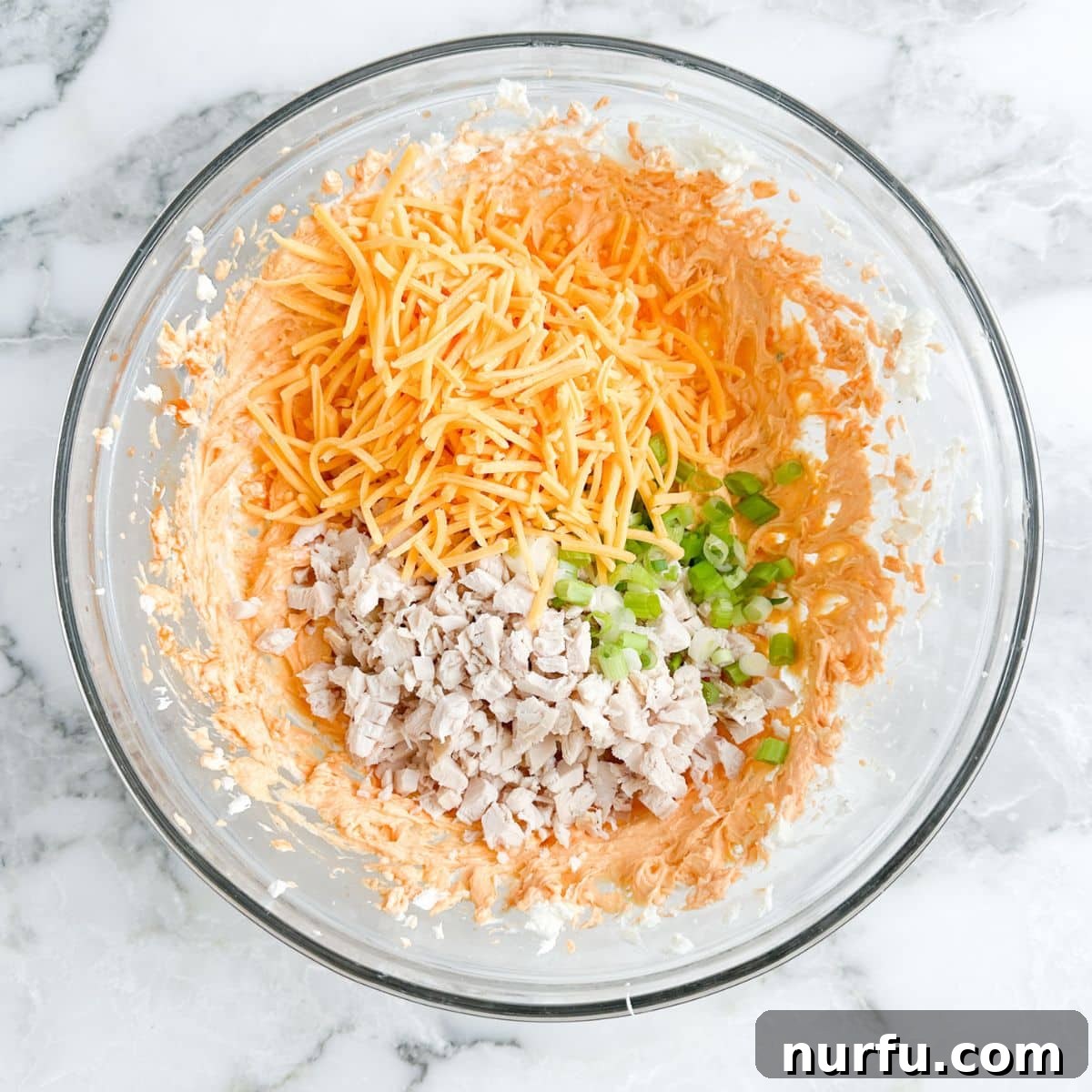 A mixing bowl filled with the cream cheese base, shredded chicken, shredded cheese, and diced green onions, stirred together to form the pinwheel filling.