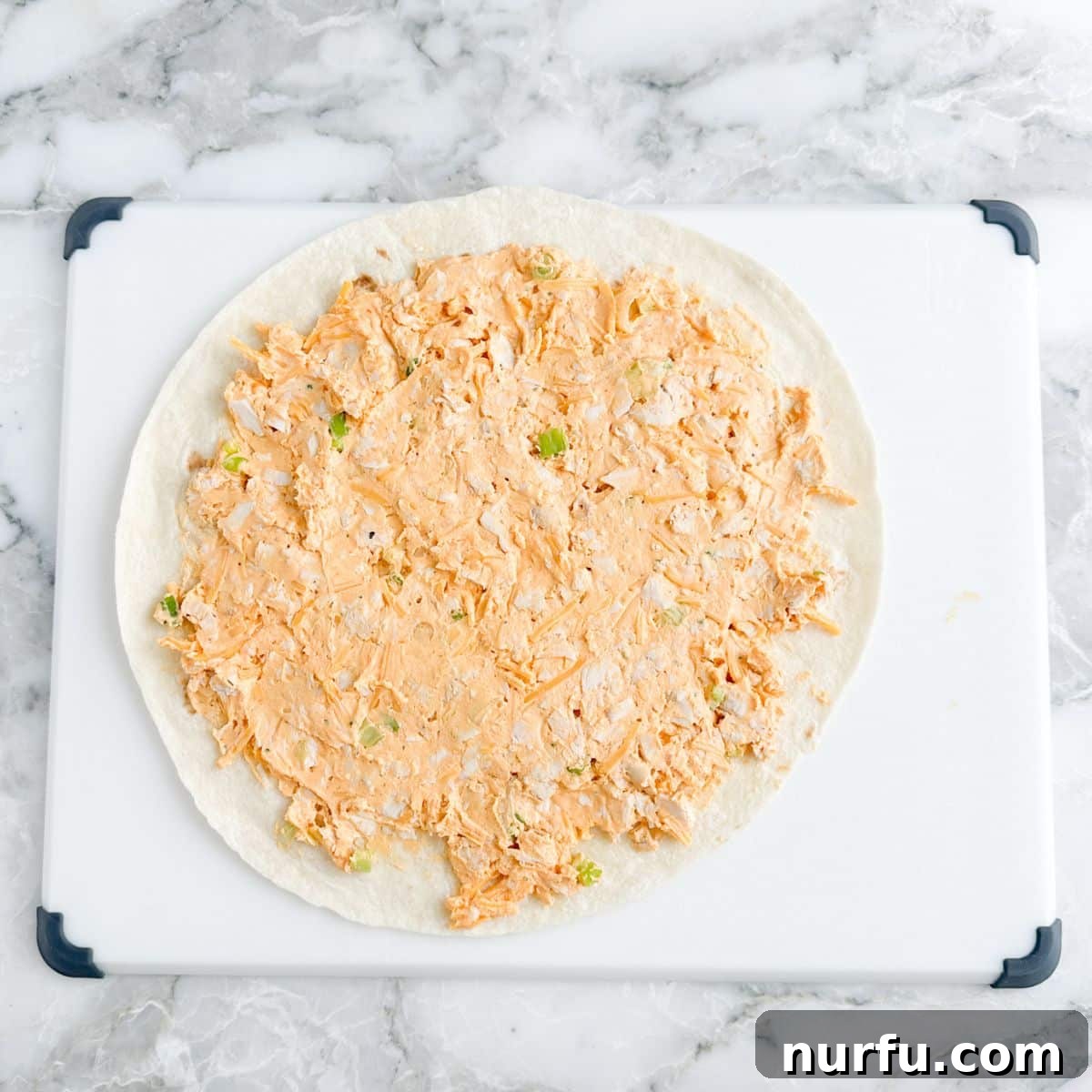 A large flour tortilla spread evenly with the buffalo chicken cream cheese mixture, covering the entire surface.