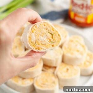 A hand presenting a perfectly sliced Buffalo Chicken Pinwheel, revealing its vibrant filling.