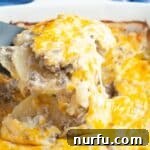 A spatula lifting sliced potatoes and melted cheese from a hearty Potato Stroganoff Casserole.