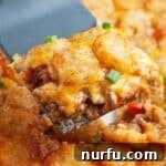 A spatula serving a piece of golden-brown tater tot casserole, showing the sloppy joe base.