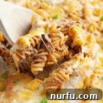 Wooden spoon scooping rotini pasta and cheese from a vibrant Taco Twist Casserole.