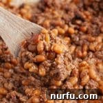 A wooden spoon serving a generous portion of rich and savory cowboy baked beans.