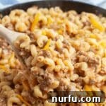 Creamy macaroni noodles with melted cheese and savory ground beef, served with a wooden spoon in a skillet.