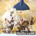 A spatula lifting a portion of cheesy ground beef and rice casserole from a baking dish.