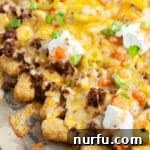 Crispy tater tot nachos generously topped with seasoned ground beef and melted cheese on a baking sheet.