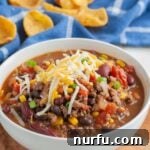 A steaming bowl of Santa Fe soup, topped with shredded cheese, featuring a rich blend of beans and ground beef.