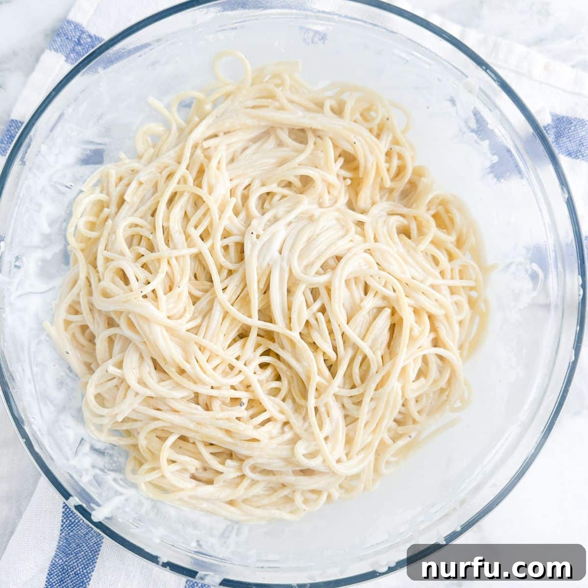 Creamy Parmesan Alfredo Spaghetti 7 A finished bowl of creamy Spaghetti Alfredo, lightly garnished with fresh parsley, sitting on a white surface, ready to be enjoyed.