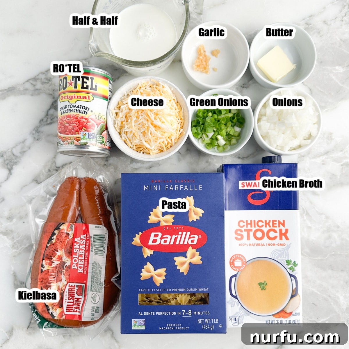 Hearty Kielbasa Pasta 3 A flat lay photograph showcasing the ingredients for one-pot kielbasa pasta: sliced kielbasa, a box of small pasta (like mini bow-ties), a can of Rotel, a carton of chicken broth, a block of cheese, an onion, and a container of half and half.
