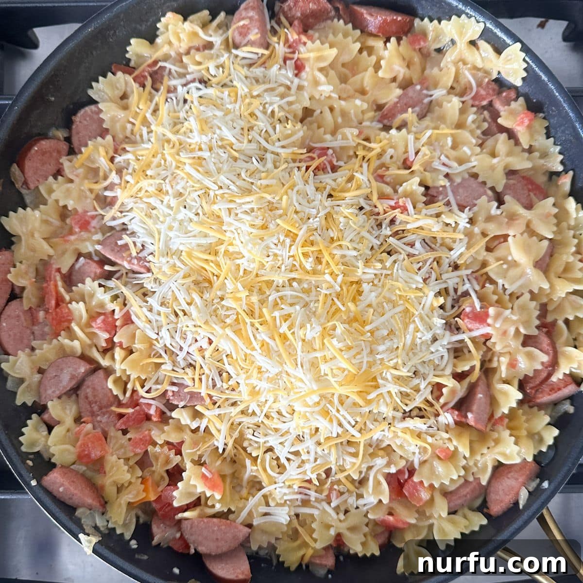 Hearty Kielbasa Pasta 6 A large skillet containing the finished kielbasa pasta dish, with shredded cheese just melted in and topped with fresh green onions, ready for serving.