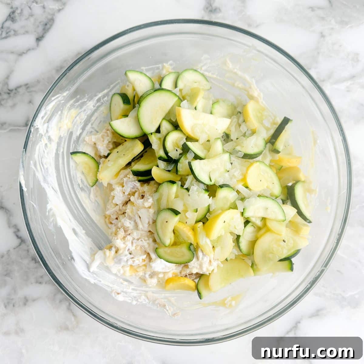 Comforting Chicken Zucchini Bake 5 A large mixing bowl filled with the creamy, savory base of the casserole: a rich blend of shredded cooked chicken, tender sautéed zucchini and yellow squash, a generous amount of shredded cheese, and creamy soup, all waiting to be combined before baking.