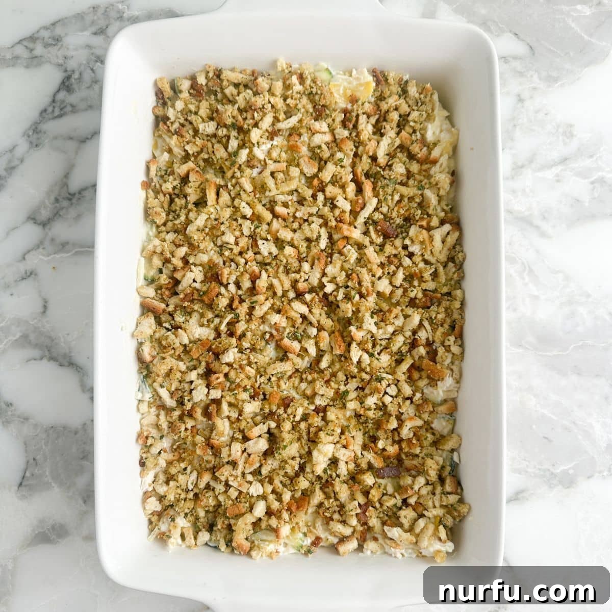 Comforting Chicken Zucchini Bake 7 A gleaming casserole dish, freshly assembled and ready for the oven, showcasing the creamy, cheesy chicken and squash base topped with a generous, golden layer of seasoned stuffing mix. The edges are neat, and the dish promises a comforting and flavorful meal.