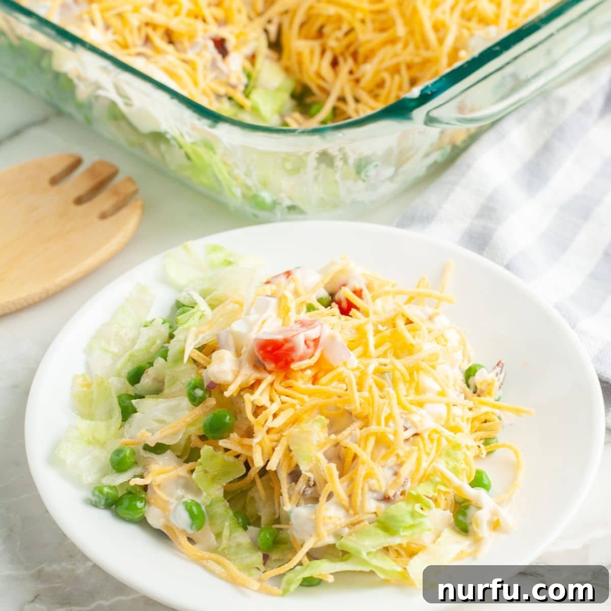 Savoring Freedom: 37 Delicious Memorial Day Recipes 19 A vibrant seven-layer salad on a white plate, showing distinct layers of lettuce, cheese, tomatoes, and other fresh ingredients.