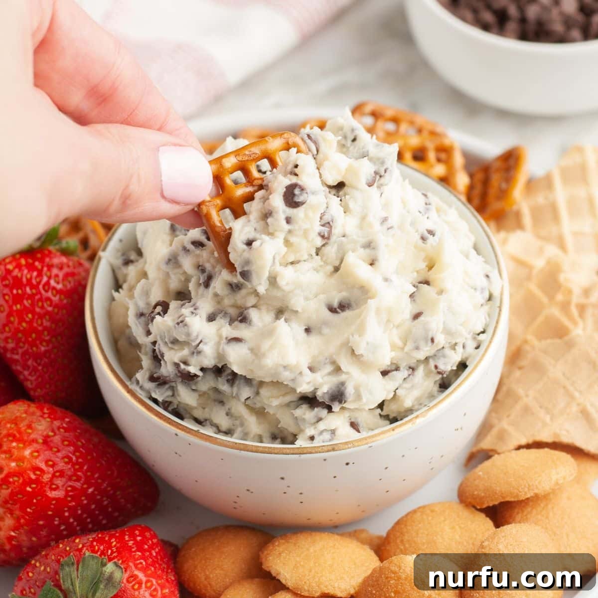 Savoring Freedom: 37 Delicious Memorial Day Recipes 34 A bowl of creamy chocolate chip cheesecake dip, served with a pretzel for dipping, offering a sweet and savory experience.
