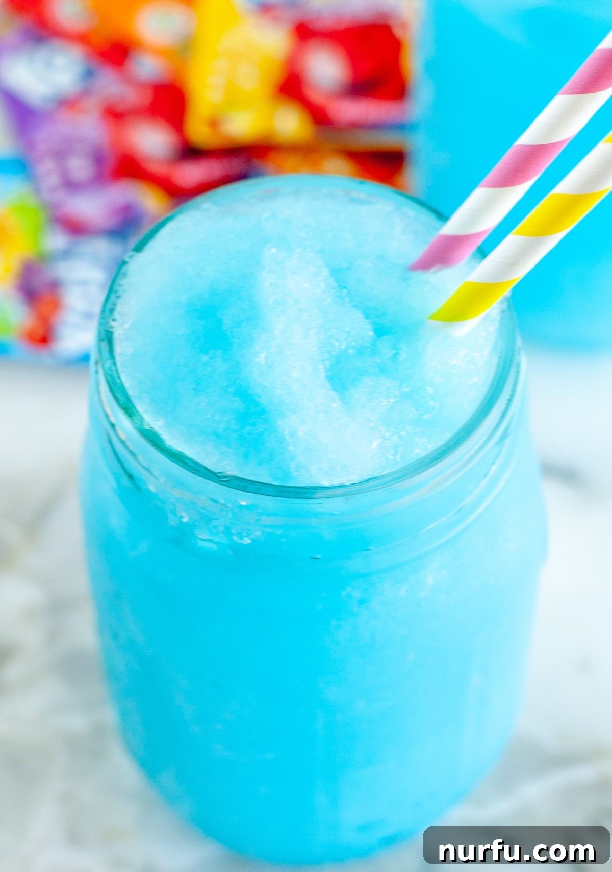 Savoring Freedom: 37 Delicious Memorial Day Recipes 39 A vibrant blue slushie in a glass, with Kool-Aid packets on the table, inviting a cool and sweet treat.