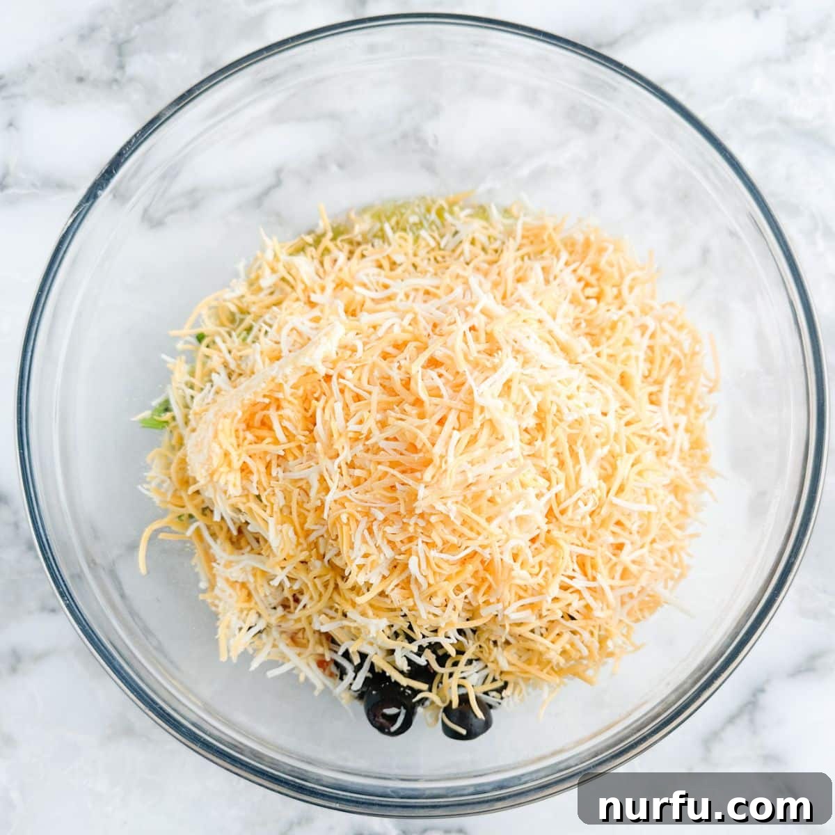 Poolside Refresh 5 A large bowl filled with the prepared poolside dip, featuring shredded cheese, black olives, and diced tomatoes, stirred together and ready to serve.