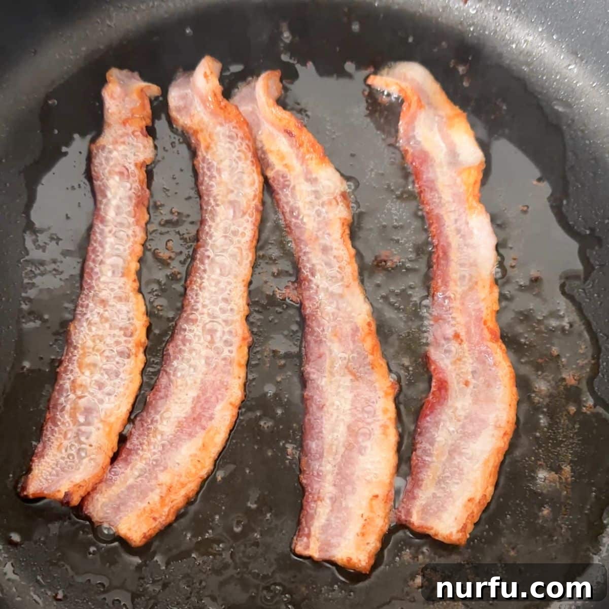 Bacon strips sizzling in a skillet.