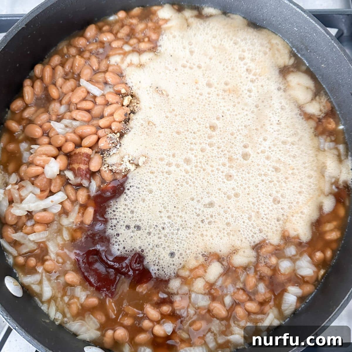 Skillet filled with baked beans, diced onion, and root beer, ready to be stirred.