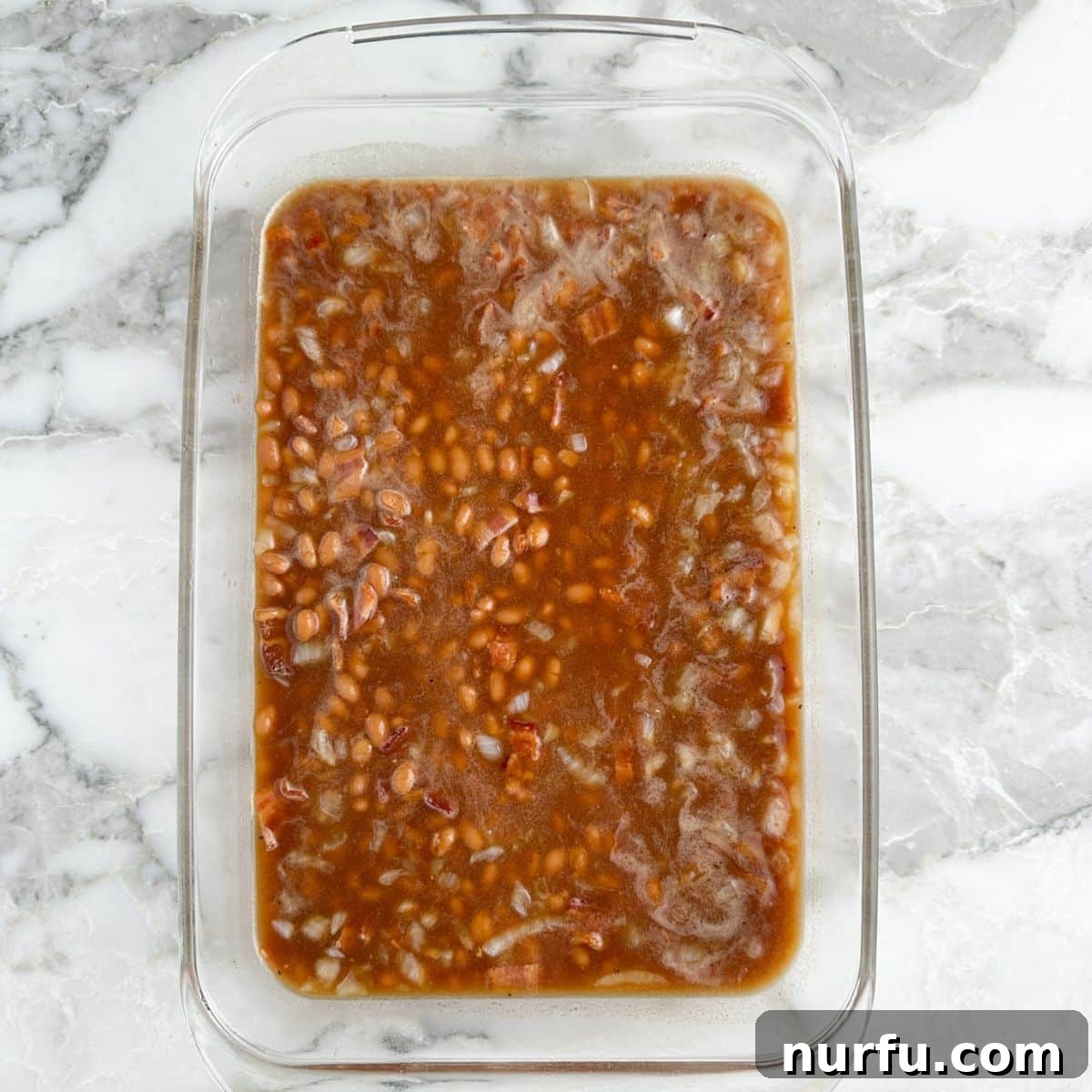 Casserole dish with baked beans after being spread evenly.