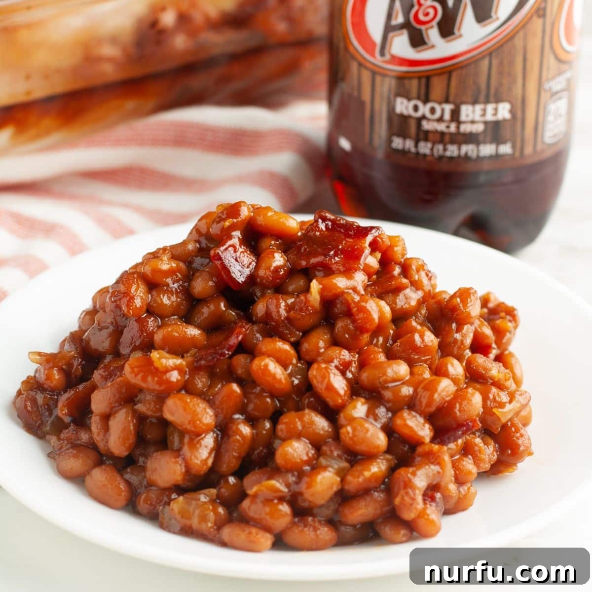 Plate of baked beans with a bottle of root beer in the background.