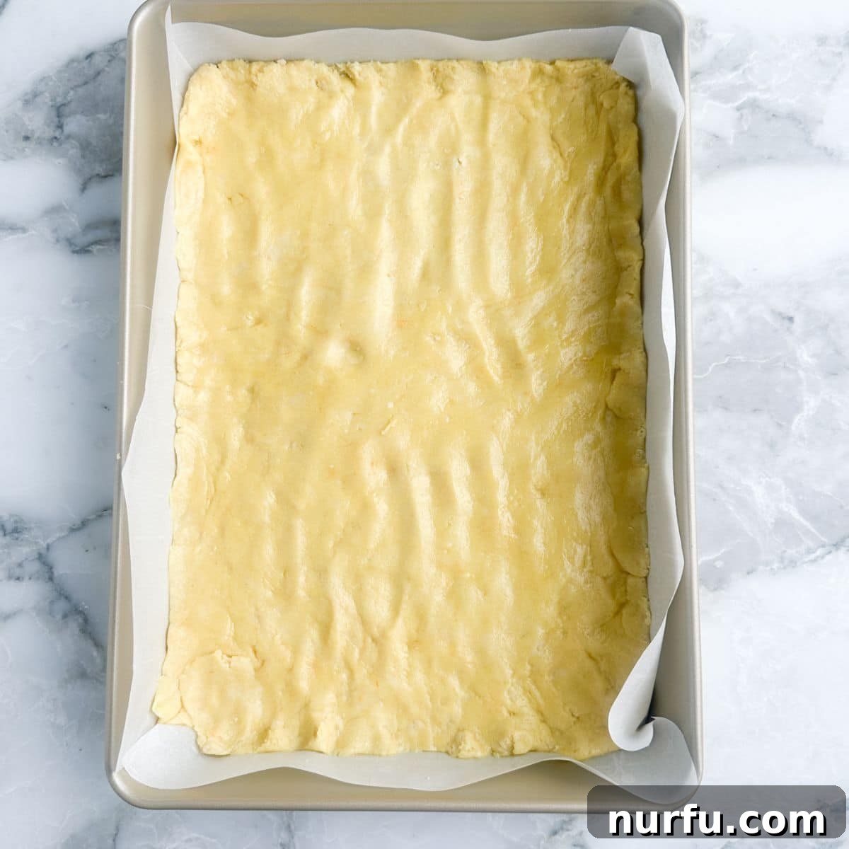 The cake mix crust expertly spread and pressed into a 9x13 baking dish, forming a solid base.
