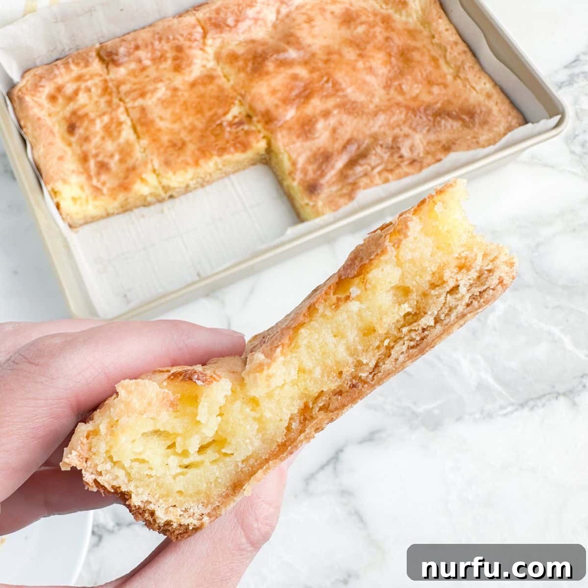 A hand carefully holding a single, perfectly cut chess square, showcasing its golden crust and creamy filling.