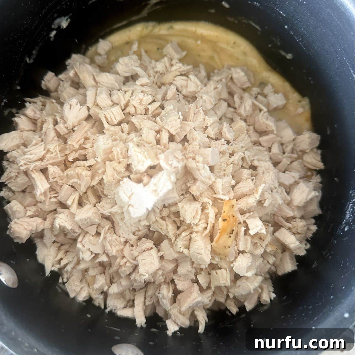 Crispy Golden Chicken Croquettes 6 Cooked, shredded chicken being stirred into the creamy, seasoned mixture in a saucepan.