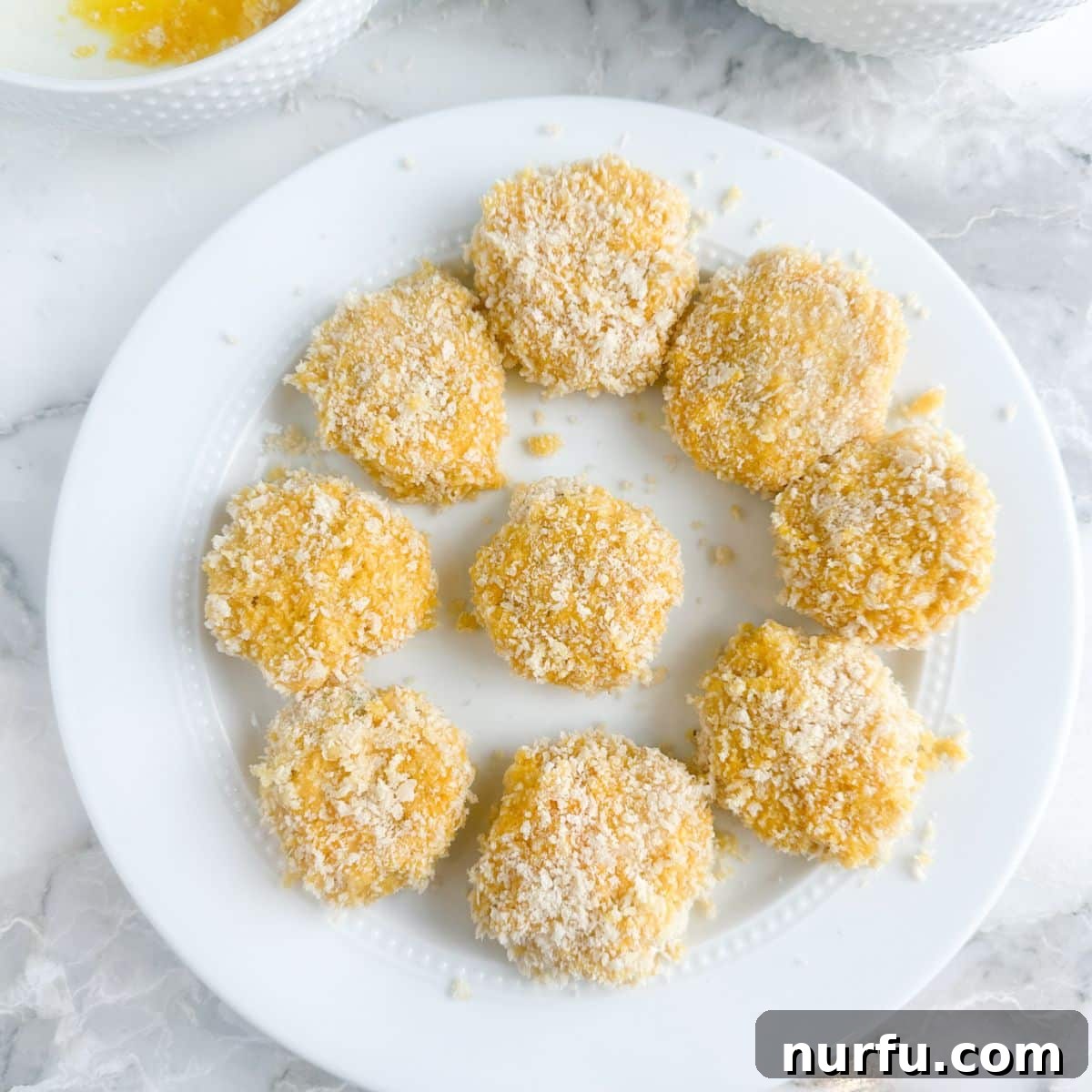 Crispy Golden Chicken Croquettes 8 A plate of uncooked chicken croquettes, fully breaded and ready for frying.