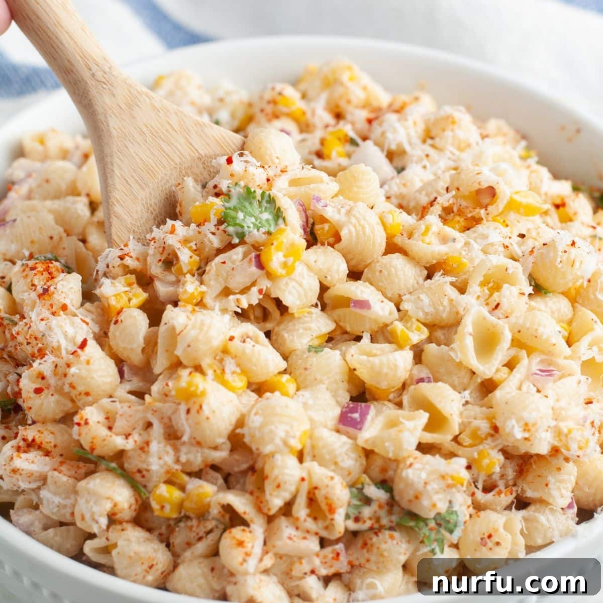 Elote Fiesta Pasta 2 A vibrant bowl of Elote Pasta Salad garnished with fresh cilantro and a wooden spoon, ready to be served.