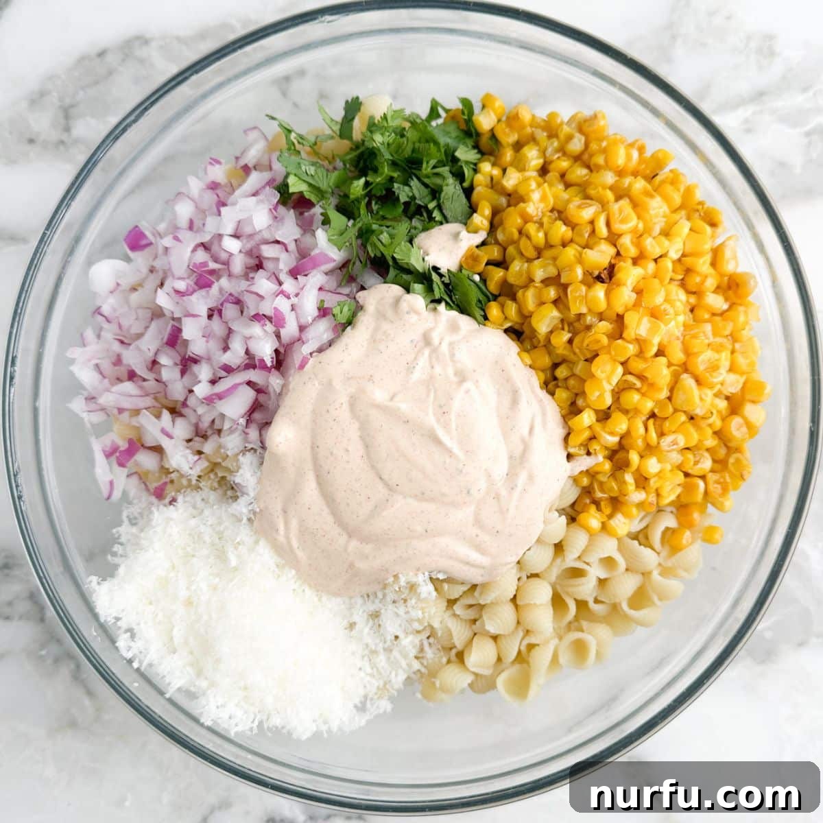 Elote Fiesta Pasta 6 A large bowl filled with uncooked pasta, corn, fresh cilantro, red onions, and cotija cheese, with a creamy dressing poured over, awaiting the final toss.