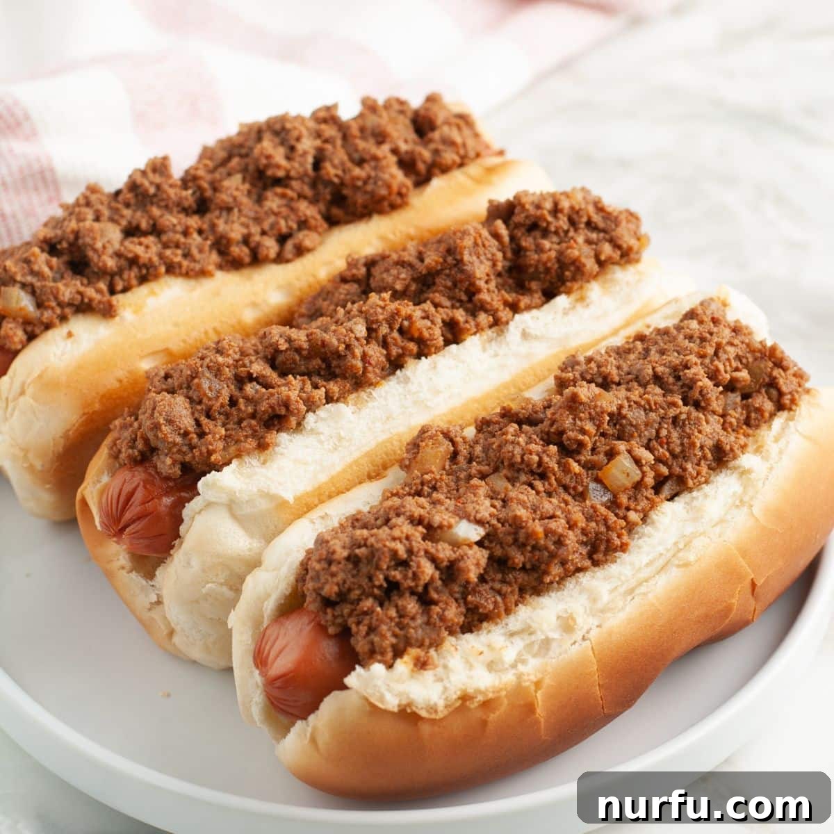 Ultimate Chili Dog Sauce 2 Plate of three chili dogs, perfectly topped with savory homemade chili and finely diced onions.