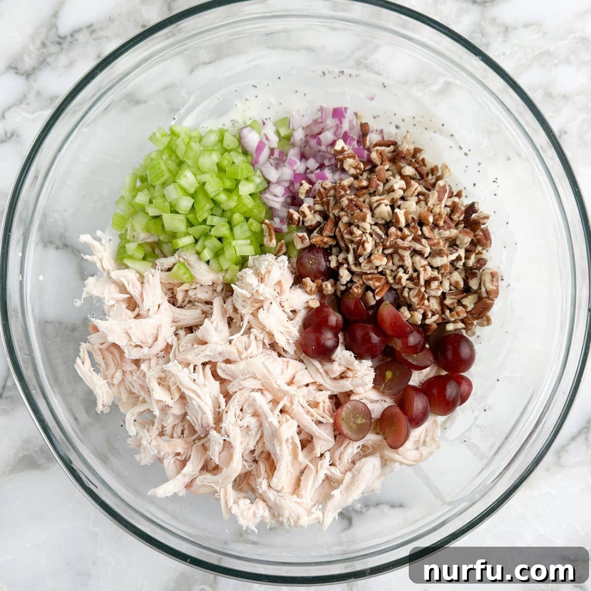 Homemade Sonoma Chicken Salad 5 A large mixing bowl filled with the vibrant ingredients for Sonoma chicken salad: shredded chicken, crisp diced celery, toasted pecans, juicy red grapes, and finely chopped red onions, ready to be tossed with the dressing.
