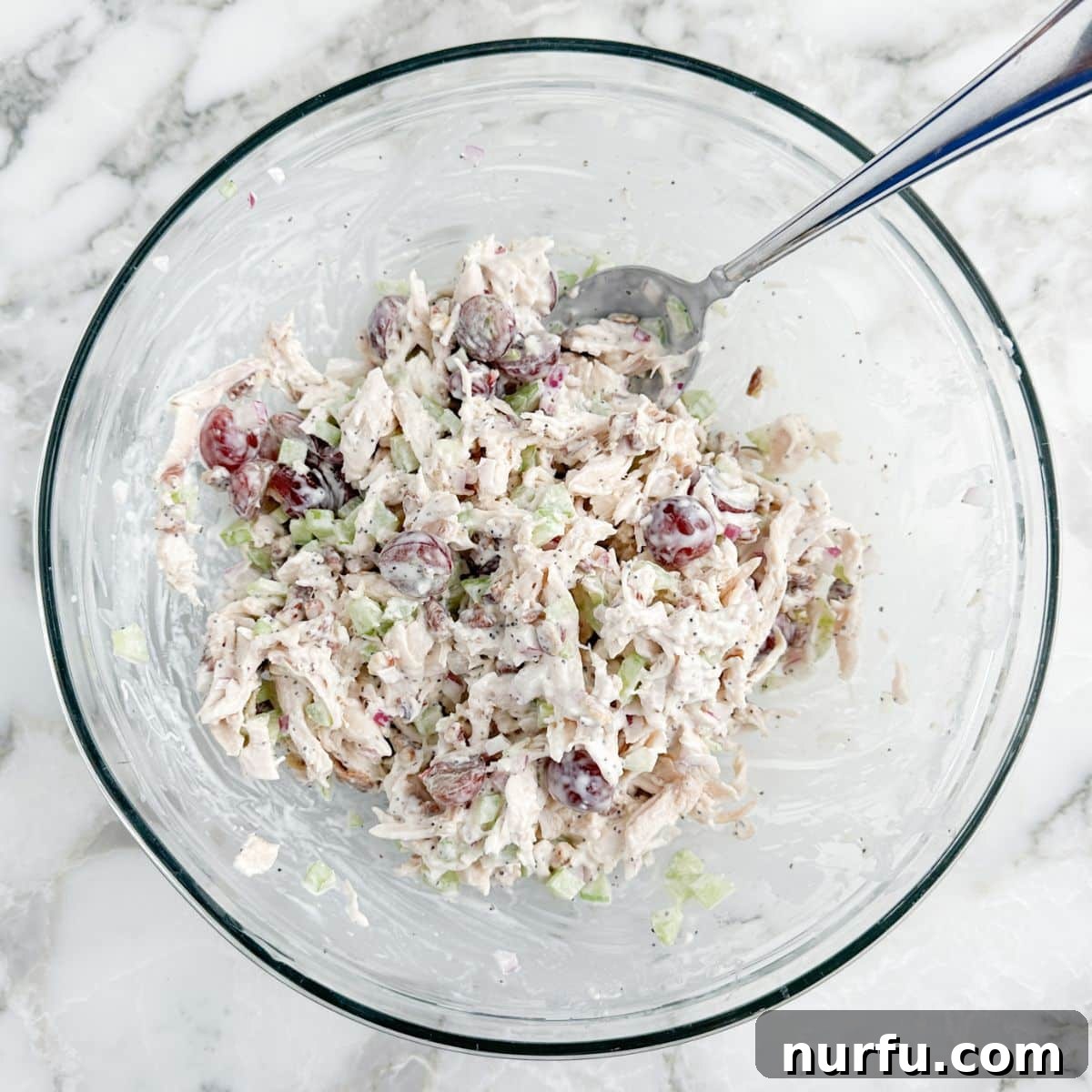 Homemade Sonoma Chicken Salad 6 A beautifully mixed bowl of Sonoma chicken salad with a serving spoon, showcasing its creamy texture, vibrant colors, and chunky ingredients.